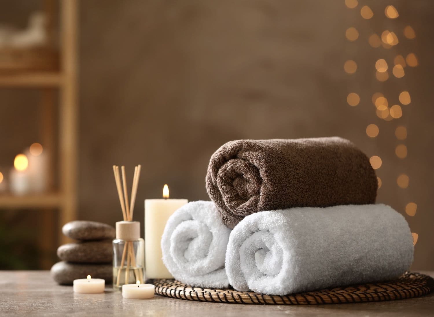 Rolled towels, spa stones and a candle set up at a soothing spa.